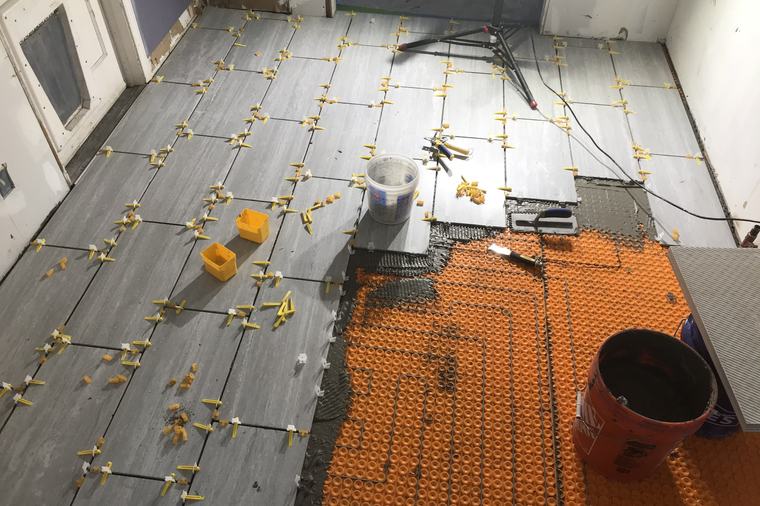 A tile floor going down over an uncoupling membrane, with leveling clips holding each tile flush