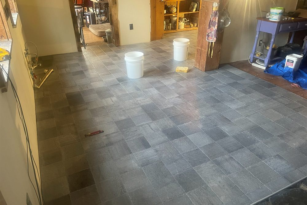 A finished slate floor laid across a kitchen and through the doorway beyond